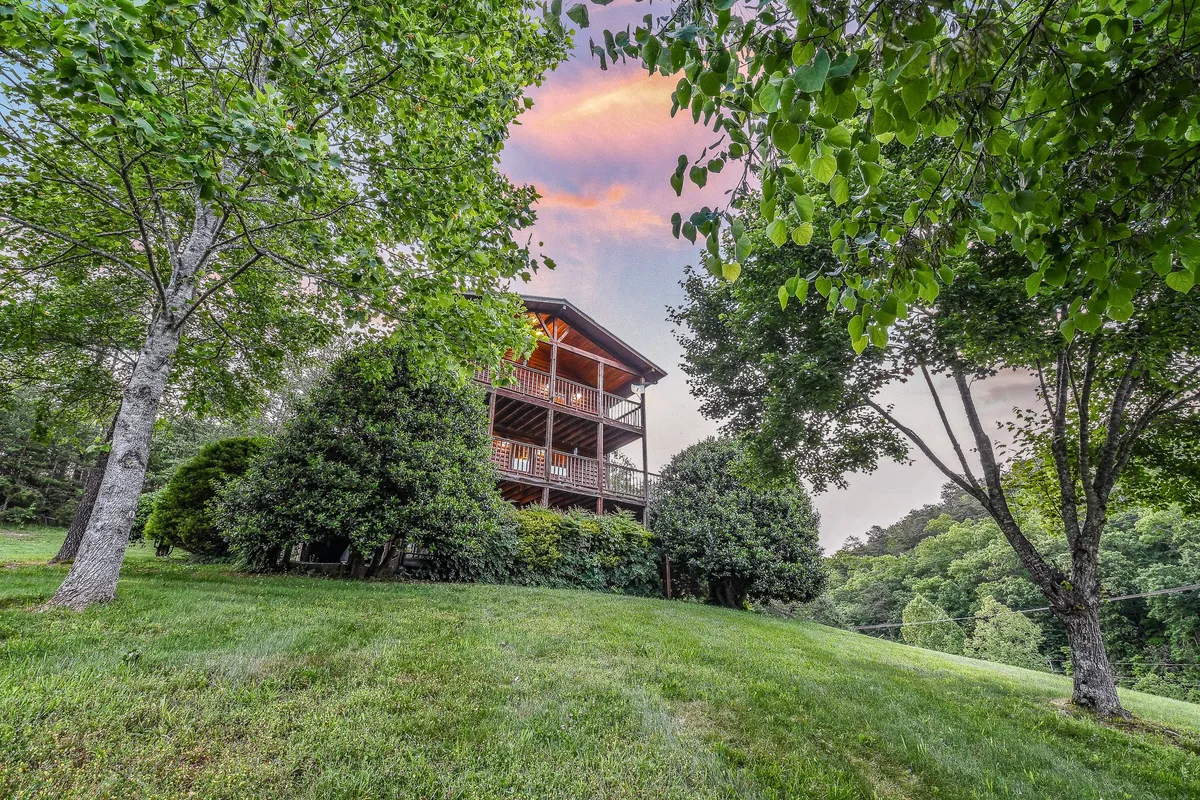 This image highlights a large wooden house nestled among green trees, with a lush lawn in the foreground. The peaceful setting invites outdoor gatherings, nature walks, and time spent together enjoying the natural environment.