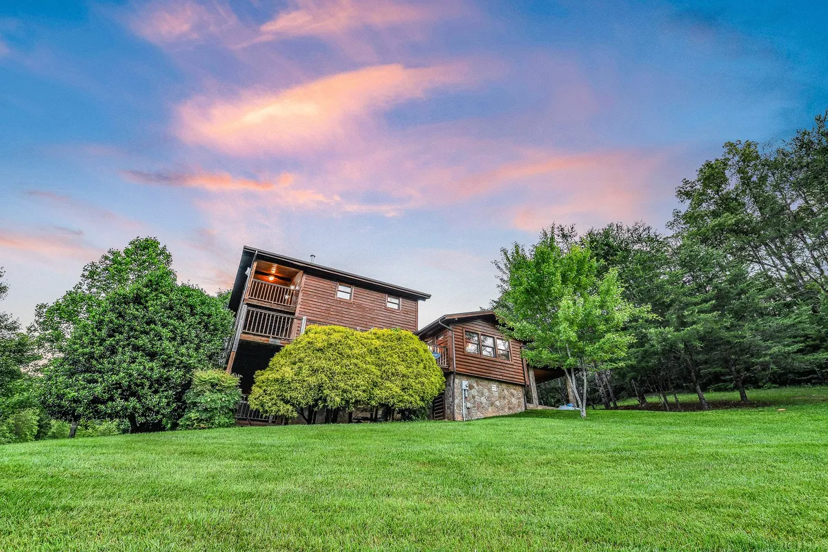 This image features the Ranch's welcoming exterior, with a lush green lawn, a charming house, and tall trees under a colorful sky. The scene conveys both the privacy and expansiveness of the secluded 6-acre property.