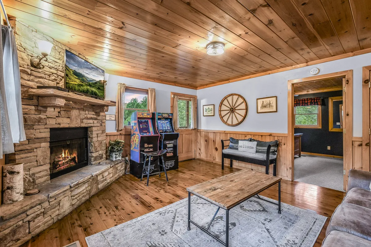 A lively interior space featuring a fireplace, a slot machine, and a wooden table. The room is set up for both relaxing and playful late-night entertainment, with cozy seating around the fire and a game area for friends to enjoy.