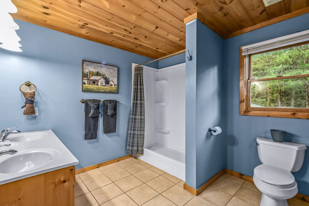 A stylish bathroom with a double sink vanity, framed artwork, a towel rack, and a glimpse of the shower area. The space is thoughtfully designed, offering both function and comfort, and has a calm, cozy ambiance for moments of self-care.