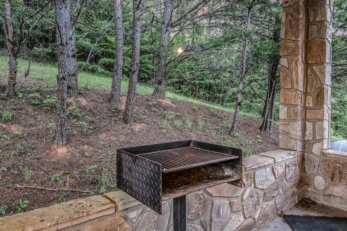 A charcoal grill sits on a stone patio surrounded by trees, ready for outdoor cooking. The relaxed scene suggests shared meals, laughter, and fresh air, perfectly capturing the ease of hosting BBQs or grilling for family and friends on the deck.