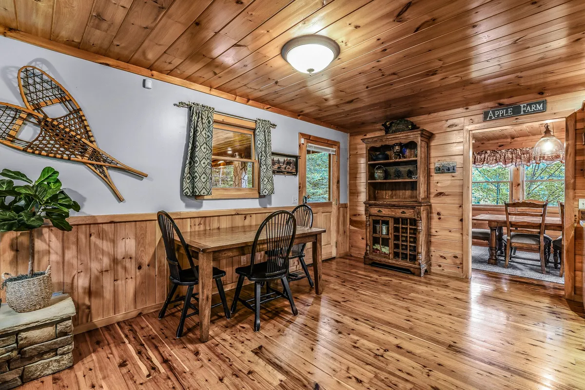 A spacious dining area with a large wooden dining table surrounded by black chairs, decorative wall accents, and stone planters. The arrangement invites large groups to gather for meals, games, or celebrations, with natural light filtering in from nearby windows.