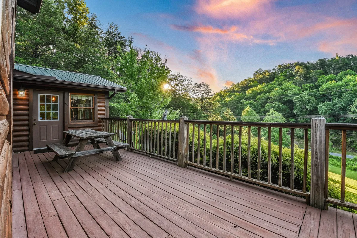 This image depicts a spacious deck with a picnic table set against a stunning mountain backdrop. The deck is surrounded by trees, creating a peaceful atmosphere ideal for outdoor dining, relaxing, and enjoying scenic sunset or sunrise views. The setting directly connects to the experience of enjoying meals and morning coffee outdoors.
