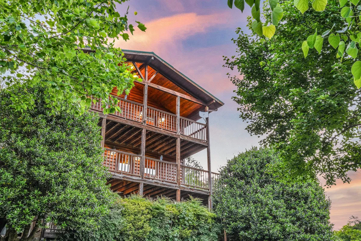 This image shows the wooden structure of the house nestled amidst lush greenery, featuring a spacious balcony that overlooks the tranquil surroundings. The natural setting and architectural design immediately evoke a sense of peace and seclusion in the Smoky Mountains.
