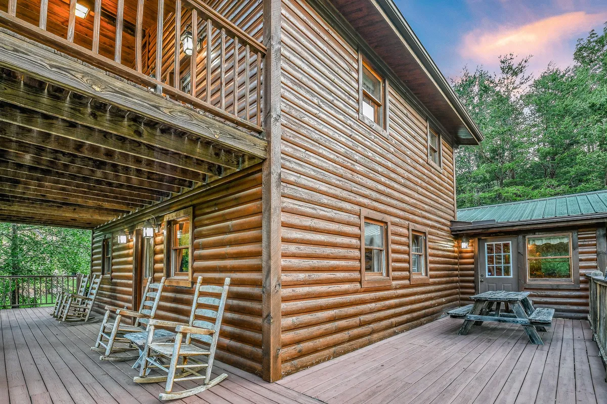 A cozy exterior view of a log cabin with a balcony, rocking chairs, and a picnic table. The balcony is perfect for social gatherings, outdoor meals, or just enjoying the mountain air. The image conveys a sense of togetherness and open-air fun, ideal for groups of friends.