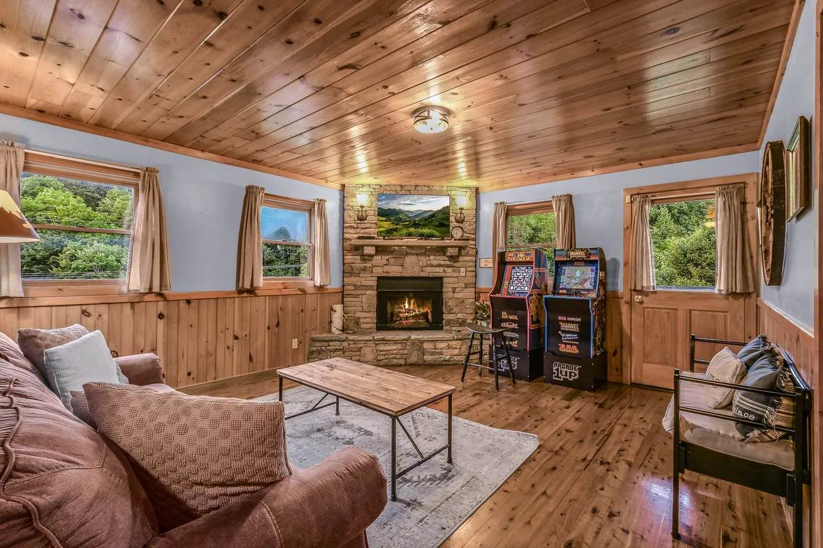 A vibrant game room showcasing a glowing fireplace, arcade games, a comfortable sofa, and a coffee table. The space is rich with nostalgic charm and tailored for both relaxation and lively entertainment.